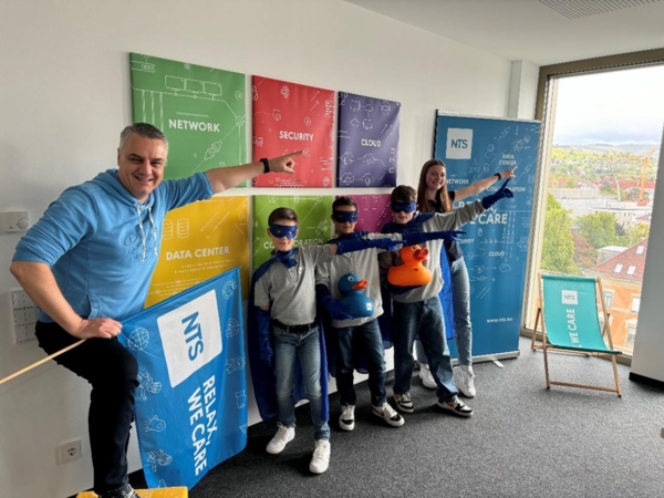 Boys'Day-Teilnehmer und Mitarbeiter mit Superheldenmasken vor Frimenplakaten